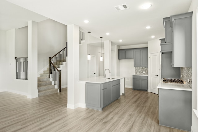 kitchen with decorative backsplash, gray cabinetry, sink, decorative light fixtures, and light hardwood / wood-style floors