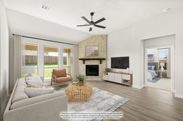 living room with ceiling fan, a stone fireplace, wood-type flooring, and vaulted ceiling