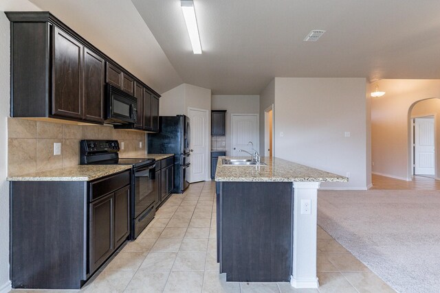 kitchen featuring light tile patterned flooring, a kitchen island with sink, light stone countertops, black appliances, and decorative backsplash