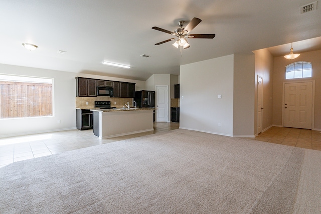 interior space featuring light colored carpet, dark brown cabinets, a center island with sink, ceiling fan, and black appliances