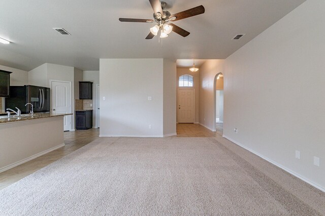 unfurnished living room with ceiling fan, sink, and light colored carpet