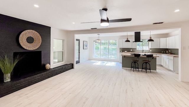 living room featuring ceiling fan, light wood-type flooring, and a brick fireplace