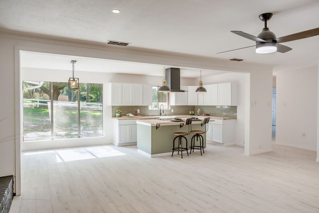 kitchen with white cabinets, backsplash, a center island, and wall chimney exhaust hood