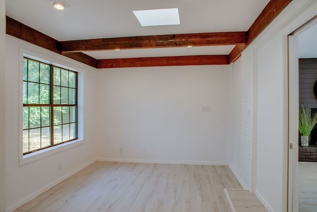 empty room with a skylight, plenty of natural light, beam ceiling, and light hardwood / wood-style floors