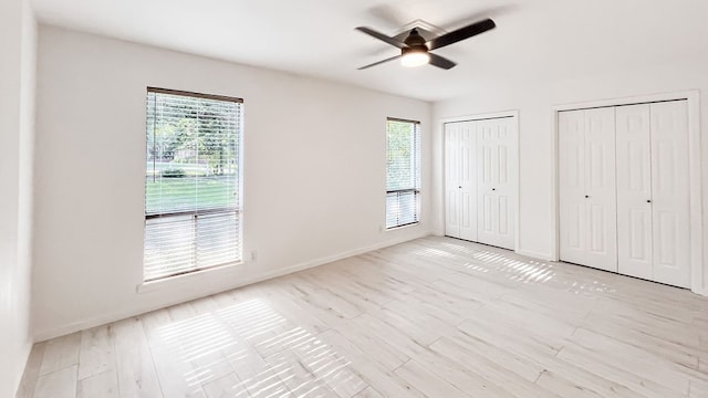 unfurnished bedroom featuring ceiling fan, light wood-type flooring, and two closets