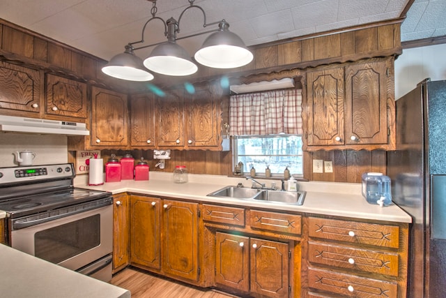 kitchen with sink, wood walls, hanging light fixtures, stainless steel appliances, and light hardwood / wood-style floors