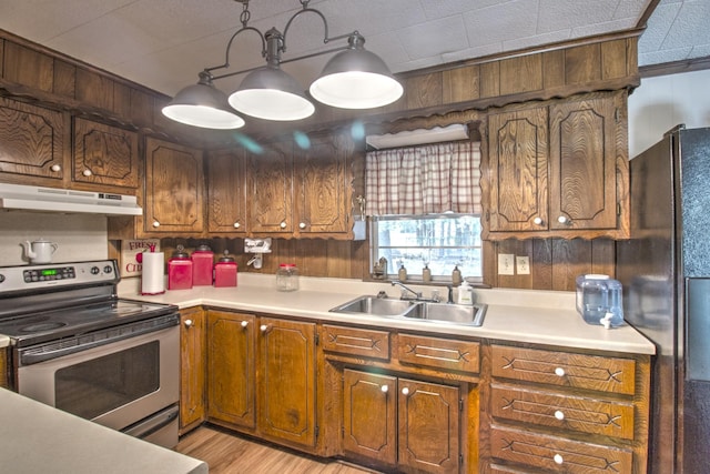 kitchen with under cabinet range hood, light countertops, stainless steel range with electric cooktop, freestanding refrigerator, and a sink