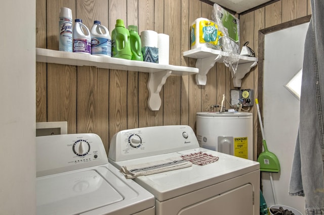 laundry area with water heater, laundry area, wood walls, and washer and clothes dryer