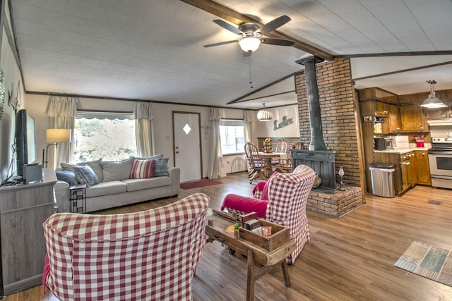 living room featuring a ceiling fan, lofted ceiling with beams, a wood stove, and light wood-style floors