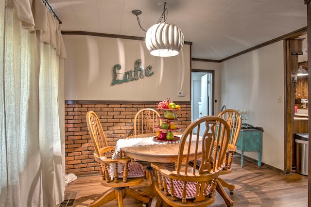 dining room featuring hardwood / wood-style flooring, ornamental molding, and brick wall