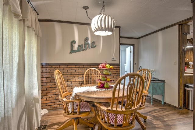 dining area featuring wood finished floors, brick wall, and ornamental molding