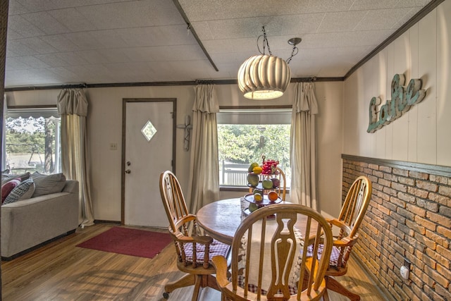 dining space with ornamental molding, brick wall, and wood finished floors