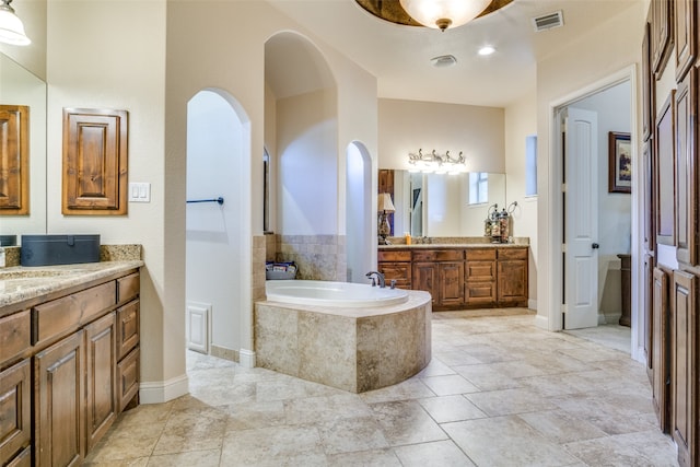 bathroom with tiled tub, vanity, and tile patterned flooring