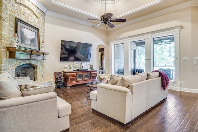 living room featuring crown molding, dark wood-type flooring, ceiling fan, and a stone fireplace