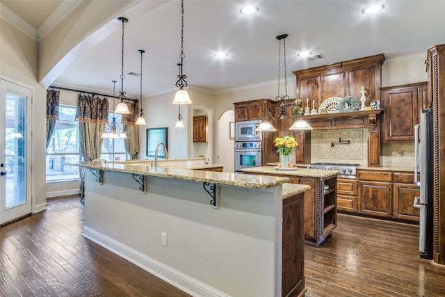 kitchen featuring a kitchen bar, light stone counters, dark wood-type flooring, hanging light fixtures, and appliances with stainless steel finishes