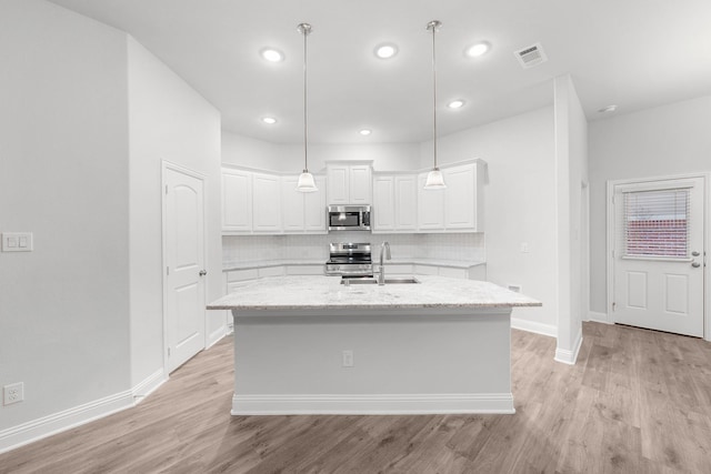 kitchen with light stone counters, stainless steel appliances, a center island with sink, white cabinets, and sink