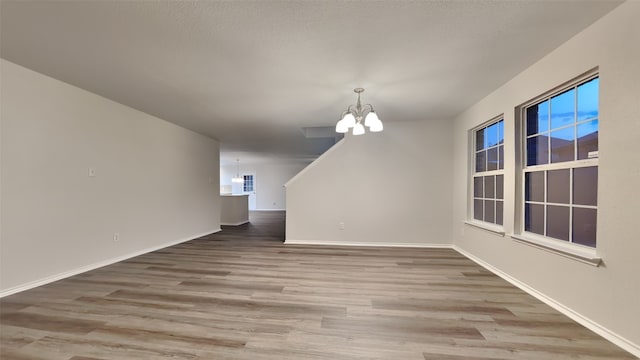 unfurnished dining area with hardwood / wood-style flooring, a textured ceiling, and an inviting chandelier