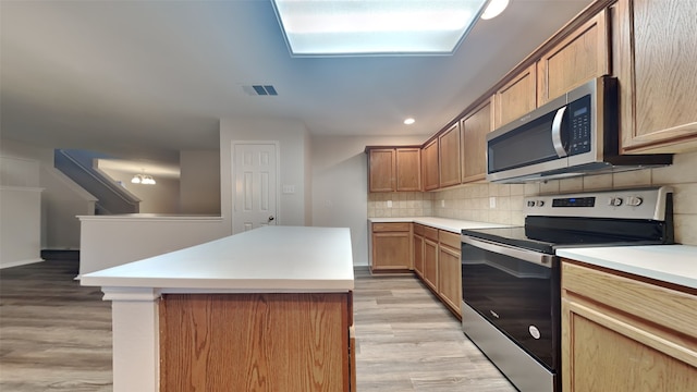 kitchen with stainless steel appliances, visible vents, light countertops, light wood-type flooring, and decorative backsplash