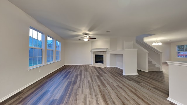 unfurnished living room with a tiled fireplace, wood-type flooring, and ceiling fan with notable chandelier