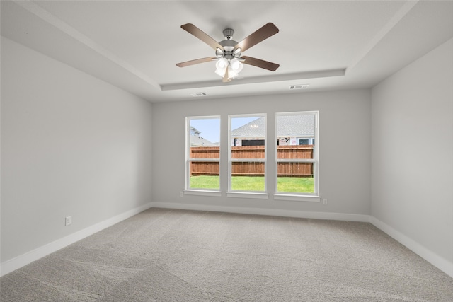 empty room with ceiling fan, carpet flooring, and a tray ceiling