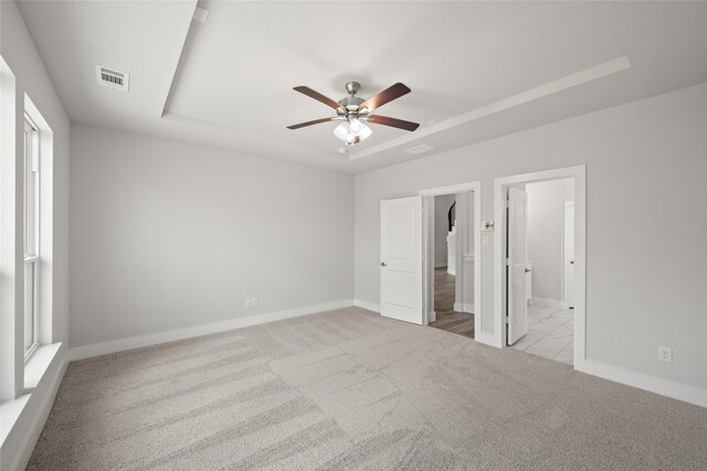 unfurnished bedroom featuring light colored carpet, a raised ceiling, ensuite bath, and ceiling fan