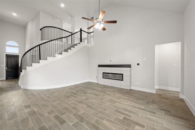 unfurnished living room featuring ceiling fan, high vaulted ceiling, a tiled fireplace, and light wood-type flooring