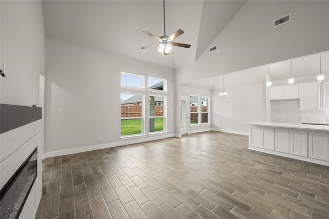 unfurnished living room featuring a fireplace, high vaulted ceiling, ceiling fan with notable chandelier, and light wood-type flooring