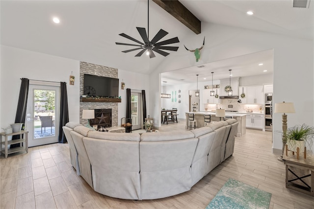 living room featuring vaulted ceiling with beams, ceiling fan, and a stone fireplace