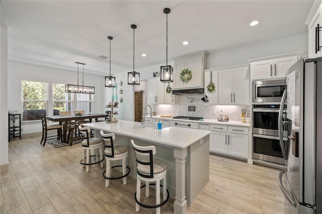 kitchen featuring a breakfast bar, white cabinets, a center island with sink, appliances with stainless steel finishes, and decorative light fixtures