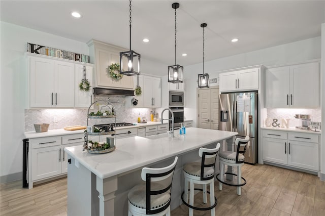 kitchen with white cabinets, pendant lighting, stainless steel appliances, and an island with sink