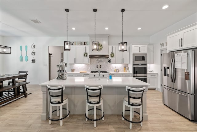 kitchen with white cabinetry, a kitchen island with sink, hanging light fixtures, and appliances with stainless steel finishes