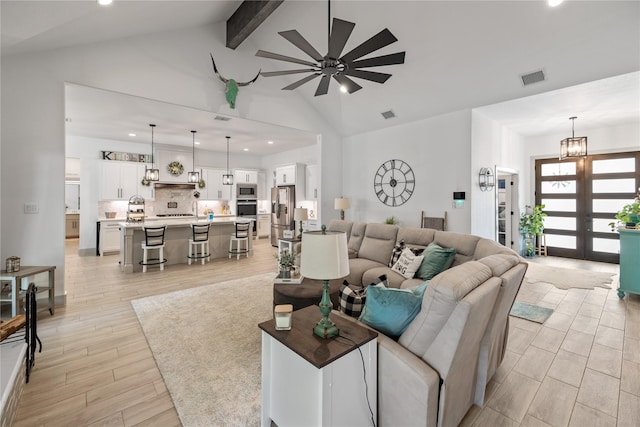 living room with ceiling fan with notable chandelier, french doors, and vaulted ceiling with beams