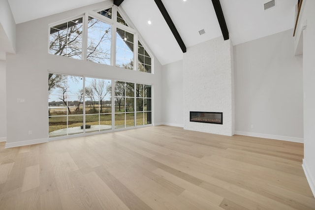 unfurnished living room featuring high vaulted ceiling, a fireplace, light hardwood / wood-style floors, and beam ceiling