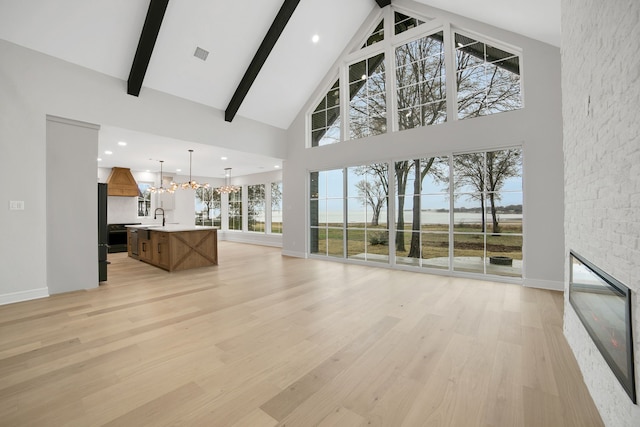 living room featuring a fireplace, beam ceiling, light hardwood / wood-style flooring, and a notable chandelier