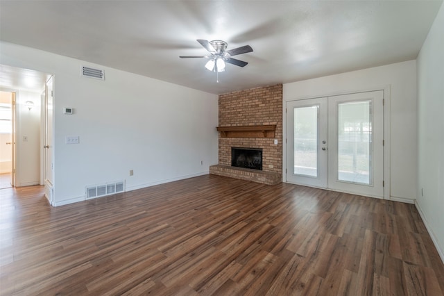 unfurnished living room with ceiling fan, french doors, dark wood-type flooring, a brick fireplace, and brick wall