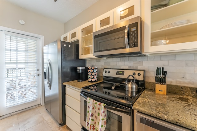 kitchen featuring appliances with stainless steel finishes, backsplash, stone counters, light tile patterned floors, and white cabinets