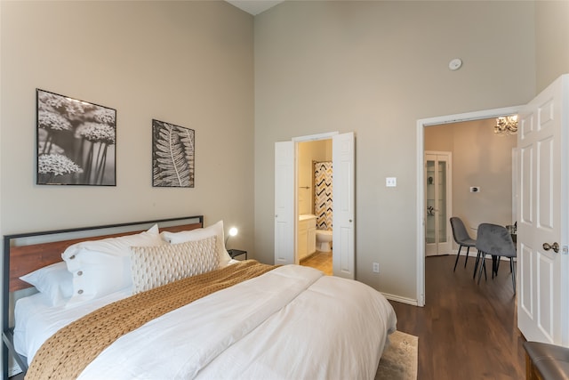 bedroom featuring a towering ceiling, a notable chandelier, ensuite bath, and wood-type flooring