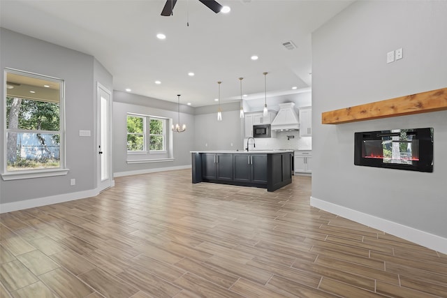 unfurnished living room featuring ceiling fan with notable chandelier, light hardwood / wood-style flooring, and sink