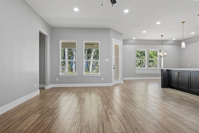 unfurnished living room with light wood-type flooring and an inviting chandelier