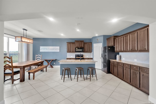 kitchen with a kitchen breakfast bar, light stone counters, black appliances, a center island with sink, and hanging light fixtures