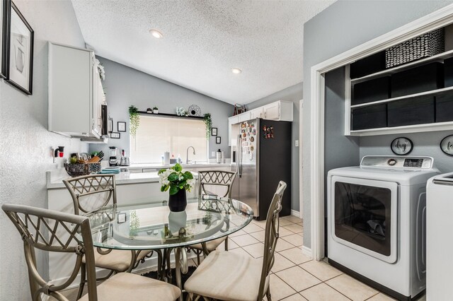 dining space featuring a textured ceiling, light tile patterned floors, independent washer and dryer, and vaulted ceiling