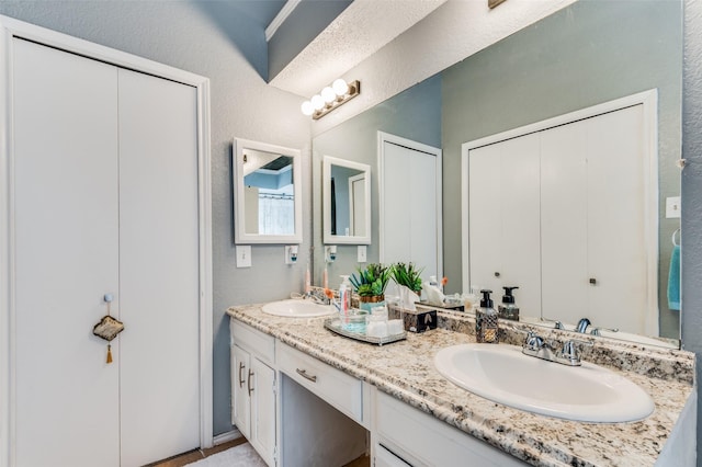 full bath with double vanity, a closet, a sink, and a textured wall