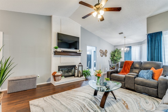 living room featuring lofted ceiling, a textured ceiling, ceiling fan with notable chandelier, a brick fireplace, and dark hardwood / wood-style floors