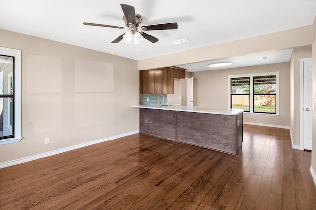 kitchen with ceiling fan, sink, kitchen peninsula, backsplash, and dark wood-type flooring