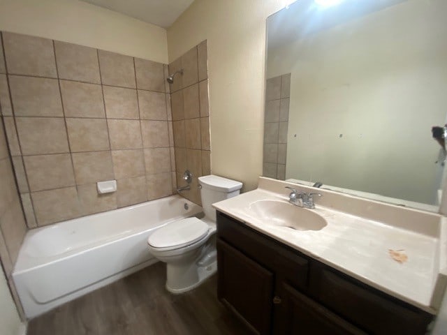 full bathroom with hardwood / wood-style flooring, vanity, tiled shower / bath, and toilet