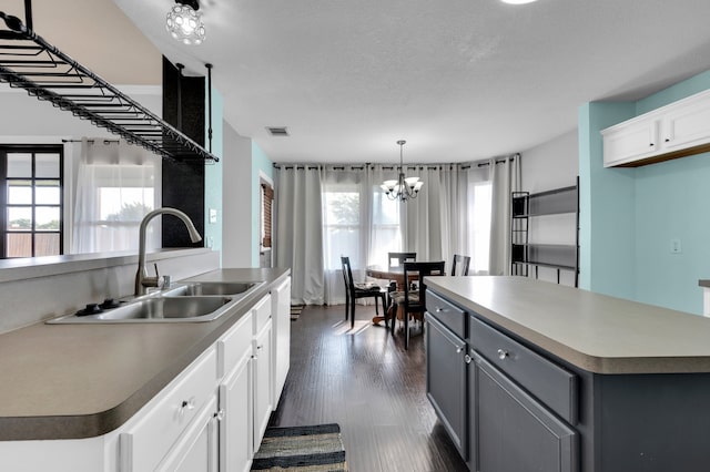 kitchen featuring a chandelier, white cabinets, dark wood-type flooring, a kitchen island, and sink