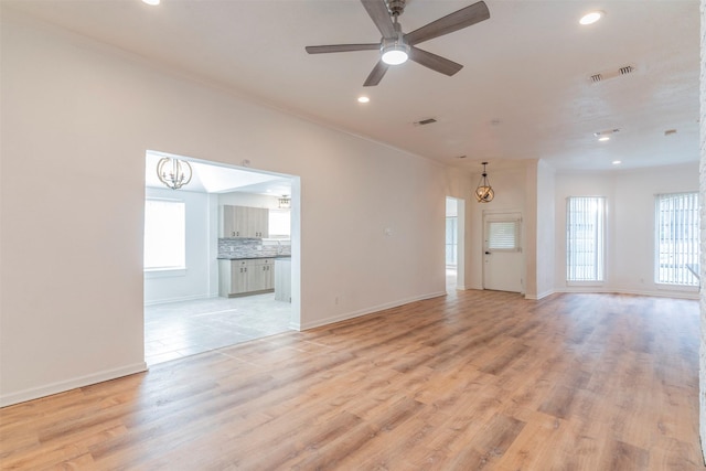 unfurnished living room with light wood-type flooring, ornamental molding, ceiling fan with notable chandelier, and a healthy amount of sunlight