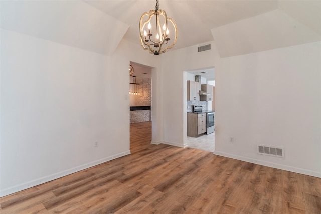 empty room featuring light hardwood / wood-style floors, brick wall, and a notable chandelier