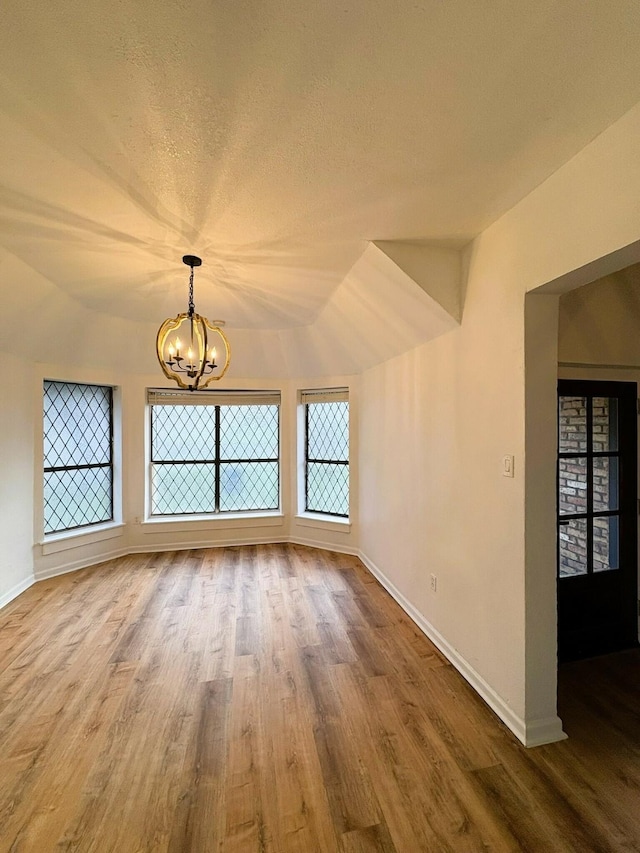 empty room with a chandelier, wood-type flooring, a textured ceiling, and vaulted ceiling