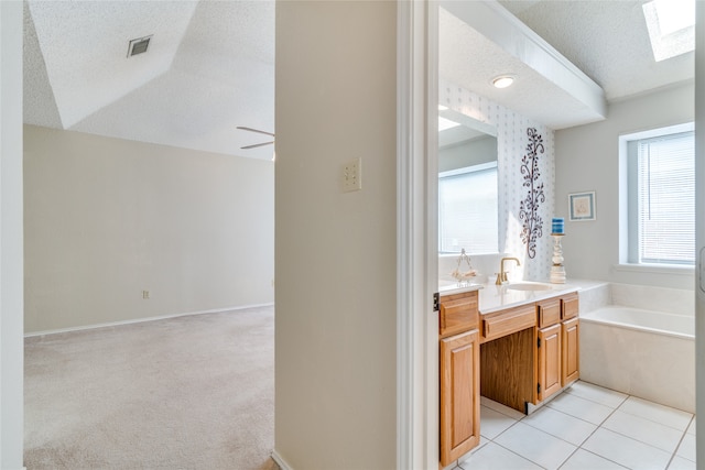 bathroom with a textured ceiling, tile patterned floors, a bathing tub, vaulted ceiling with skylight, and vanity